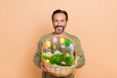 Portrait of attractive cheerful man holding in hands festal decor basket easter time isolated over...
