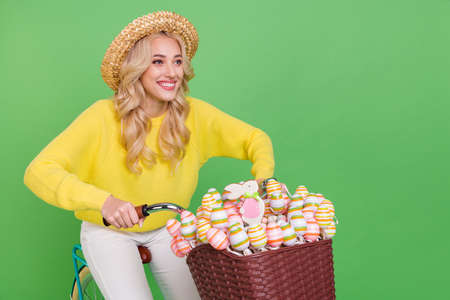 Photo of funky adorable woman wear yellow sweater cap riding bike looking empty space isolated green...