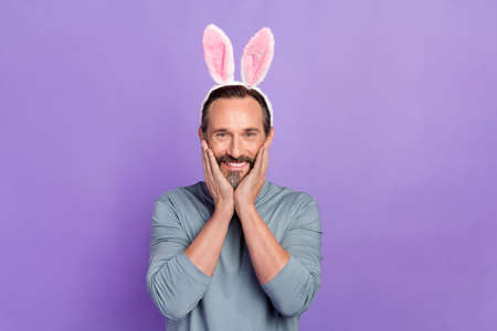 Portrait of satisfied person arms on cheeks toothy smile look camera bunny ears isolate don purple color backgroundの写真素材