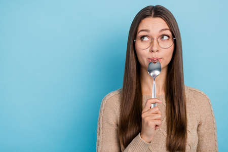 Portrait of attractive funny cute girl licking spoon thinking copy blank space isolated over bright blue color backgroundの写真素材