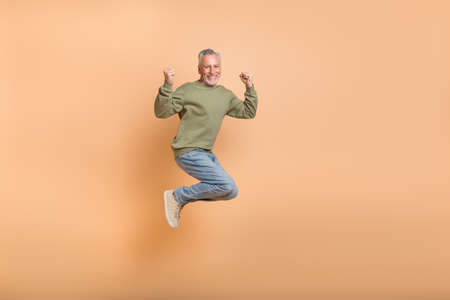 Full body photo of hooray aged grey hairdo man jump wear pullover jeans shoes isolated on beige...