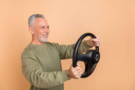 Photo of funny elder white hairdo man drive car wear grey shirt isolated on beige color backgroundの写真素材