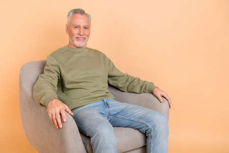 Photo of nice old grey hairdo man sit wear green pullover jeans isolated on beige color backgroundの写真素材