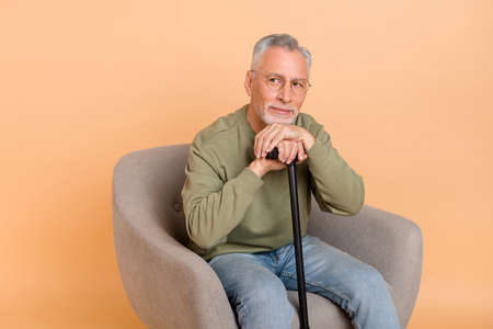 Photo of optimistic old grey hairdo man sit with stick look promo wear pullover jeans isolated on...