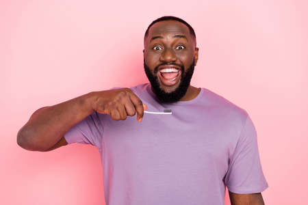 Photo of impressed funny guy dressed violet t-shirt cleaning teeth isolated pink color background