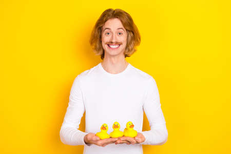 Portrait of handsome cheerful funny childish male take bath holding three little ducklings isolated...