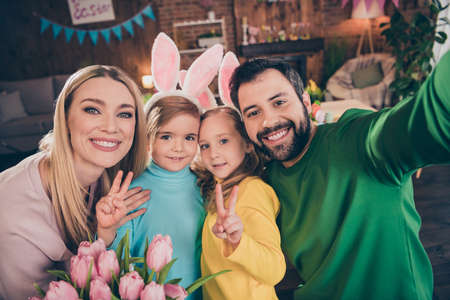 Photo of cheerful family celebrate easter husband take selfie of his wife and children showing v-sign spend time indoorsの写真素材