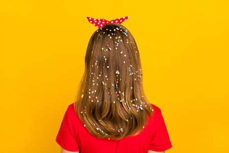 Back view photo of adorable charming little girl with long brown hair with confetti isolated on yellow color backgroundの写真素材
