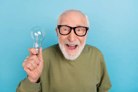 Portrait of attractive amazed cheery grey-haired man holding bulb new discovery explore isolated over bright blue color backgroundの写真素材