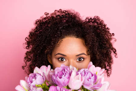 Photo of young adorable girl hiding behind spring flower watch holiday isolated over pink color...