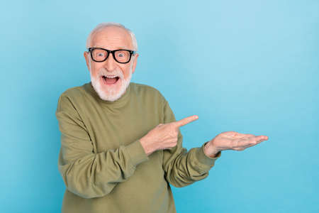 Portrait of attractive cheerful amazed grey-haired man demonstrating offer ad isolated over bright blue color backgroundの写真素材
