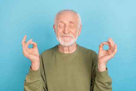 Portrait of attractive cheerful funny grey-haired man meditating free time isolated over bright blue...