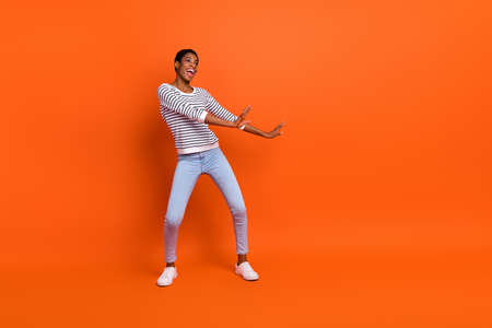 Full length photo of sweet young lady dance wear shirt jeans footwear isolated on orange background