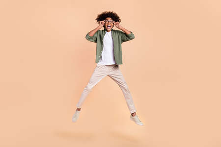 Full length body size view of attractive cheerful guy jumping touching specs isolated over beige pastel color backgroundの写真素材