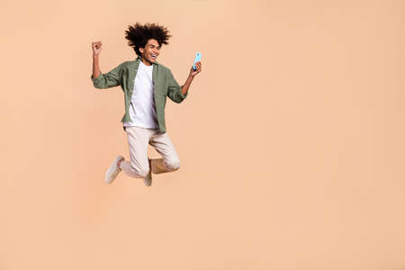 Full length body size view of attractive cheerful trendy guy jumping using cell rejoicing isolated...