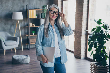 Photo of charming sweet lady pensioner holding modern device staying home office indoors workplace workstationの写真素材