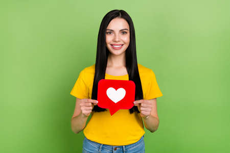 Photo of pretty cheerful lady dressed yellow t-shirt holding heart like sign isolated green color...