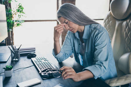 Photo of stressed depressed pensioner lady sit chair hand touch head create database office indoorsの写真素材
