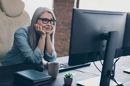 Portrait of positive pensioner lady sitting chair look screen database operation protection office indoorsの写真素材
