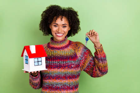 Photo of funky young curly hairstyle lady hold house key wear red sweater isolated on green color backgroundの写真素材