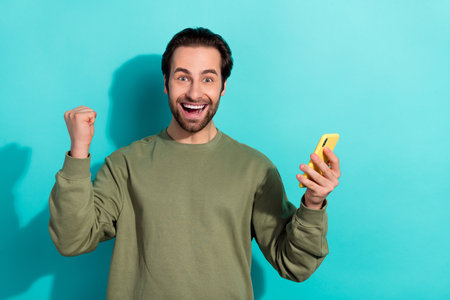Photo of cool brunet young guy hold telephone yell wear khaki sweatshirt isolated on teal color backgroundの写真素材