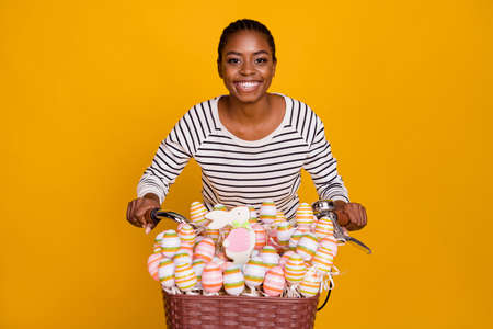 Photo of young pretty excited girl ride bicycle colorful easter eggs on sticks isolated over yellow color backgroundの写真素材