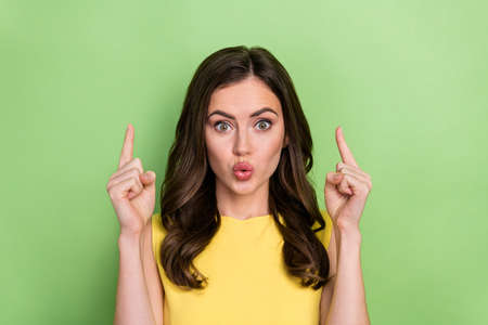 Portrait of attractive amazed girly wavy-haired girl pout lips demonstrating up copy space news isolated over bright green color backgroundの写真素材