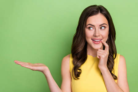 Portrait of attractive girly cheerful wavy-haired girl holding copy space deciding isolated over bright green color backgroundの写真素材