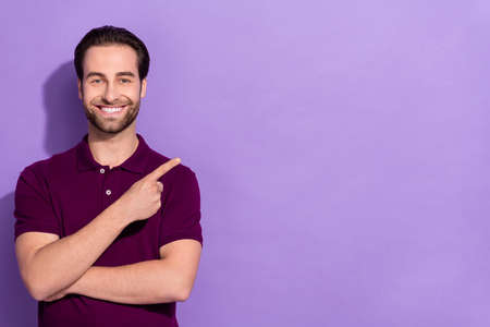 Portrait of handsome cheerful young male point finger blank space promoter recommendation isolated on violet color backgroundの写真素材