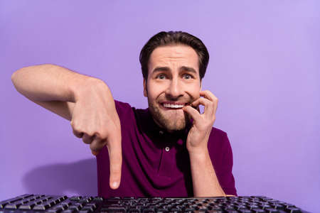Photo of stressed young brunet guy point keyboard wear violet t-shirt isolated on purple color...
