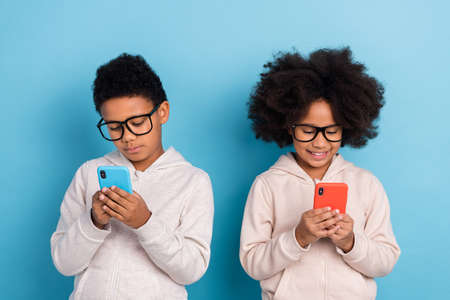 Portrait of small little friends friendship pre-teen schoolkids nerds using device chat isolated over bright blue color backgroundの写真素材