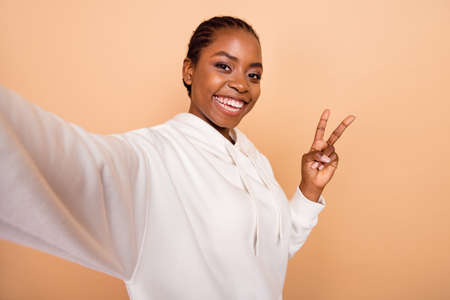 Photo of positive charming person take selfie fingers make v-sign isolated on beige color backgroundの写真素材