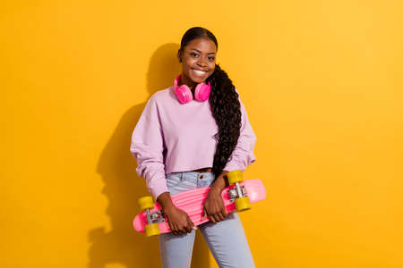 Photo of friendly positive attractive person hold skateboard enjoy free time isolated on yellow color backgroundの写真素材