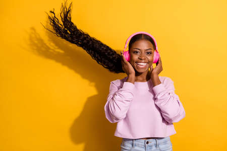 Portrait of positive carefree lady hands touch earphones toothy smile look camera isolated on yellow color backgroundの写真素材