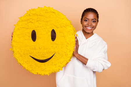 Photo of charming positive girl hold large emoticon paper collage isolated on beige color backgroundの写真素材