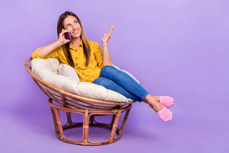 Full size photo of adorable dreamy female relaxing on comfy armchair talking with best friend isolated on violet color backgroundの写真素材