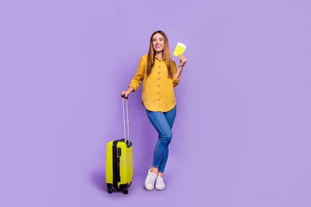 Full length image of lovely girl in airport waiting for her flight hold luggage and tickets isolated on violet color backgroundの写真素材