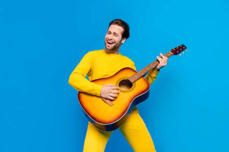 Portrait of attractive cheerful guy playing guitar singing having fun isolated over bright blue...