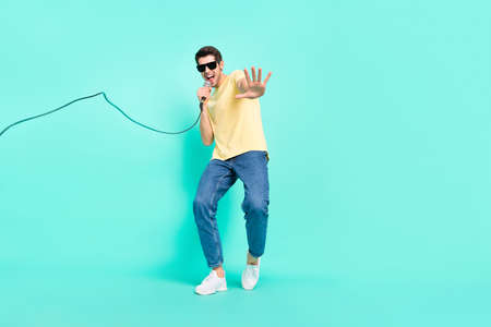 Full size photo of funny brunet young guy sing wear eyewear t-shirt jeans sneakers isolated on teal backgroundの写真素材