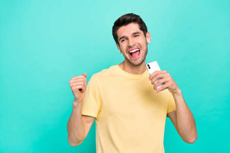 Photo of cool brunet millennial guy sing telephone wear t-shirt headphones isolated on teal color backgroundの写真素材