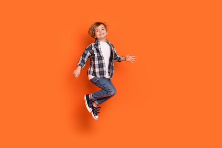 Full size profile side photo of young cheerful boy have fun jump up isolated over orange color backgroundの写真素材