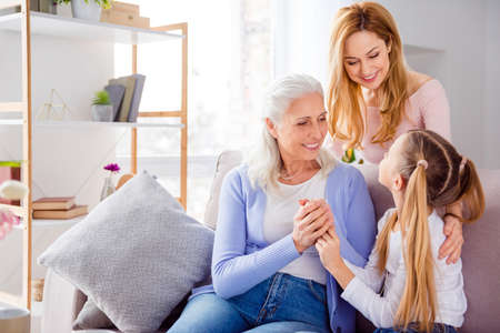 Photo of three idyllic cheerful people sitting couch hold hands communicate free time indoorsの写真素材