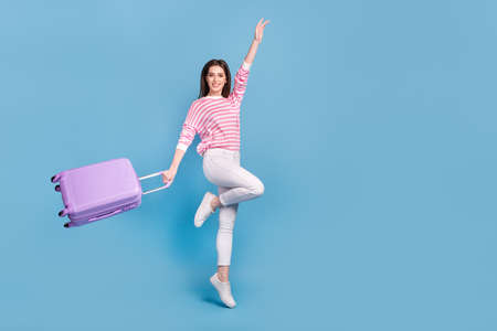 Full body portrait of cheerful gorgeous lady hold bag raise hand enjoy summer isolated on blue color backgroundの写真素材