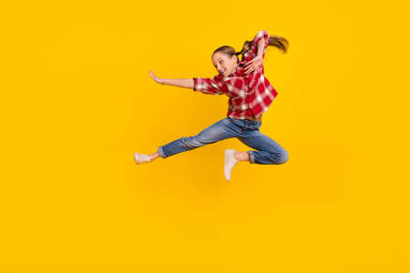 Photo of cool shiny schoolkid dressed plaid shirt jumping high practicing karate isolated yellow...