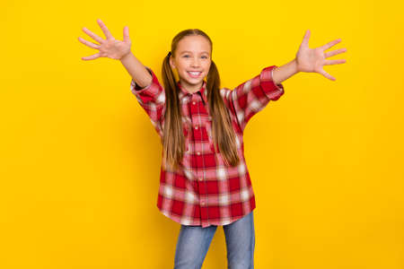Photo of charming impressed schoolgirl wear checkered shirt ready embrace you open arms isolated yellow color backgroundの写真素材