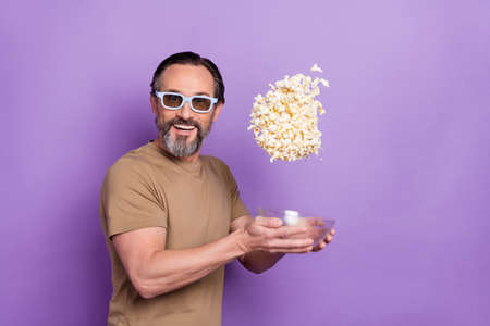 Photo of cheerful man ordering pop corn watching 3d film in cinema during vacation isolated on purple color backgroundの写真素材