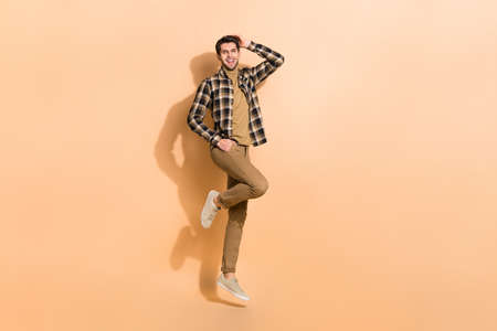 Full length body size view of attractive cheerful guy jumping posing having fun isolated on beige...