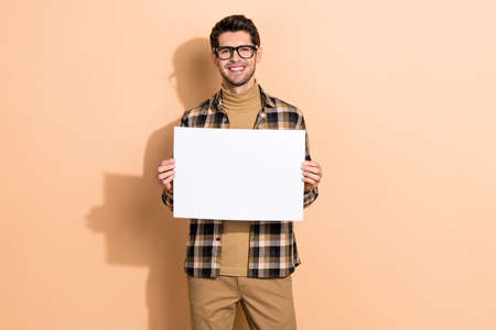 Portrait of attractive cheerful guy specialist holding in hands copy space banner isolated over beige pastel color backgroundの写真素材