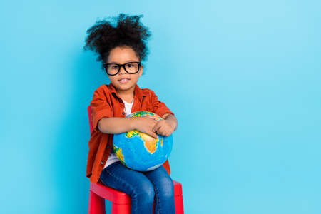 Photo of good mood emotion casual wear little girl relaxing learning our planet isolated on blue...
