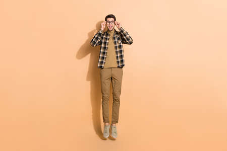 Full length body size view of attractive cheerful guy jumping touching specs isolated on beige...
